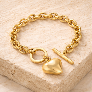 Gold chain bracelet with a heart charm on a beige stone surface