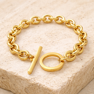 Gold chain bracelet with a unique clasp on a beige stone surface