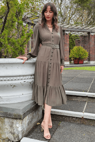 Woman in a long, sage green dress standing outdoors on stone steps.